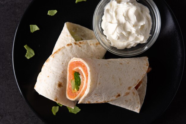 Rollo de sándwich de envoltura de salmón con queso y verduras sobre fondo de pizarra negra