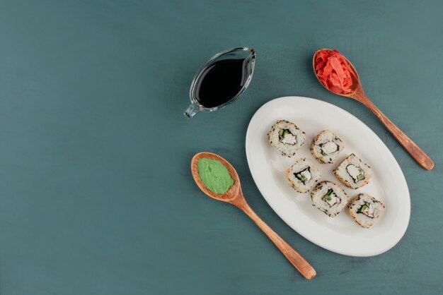 Rollo de sushi de Alaska en un plato blanco con wasabi, jengibre encurtido y salsa de soja.