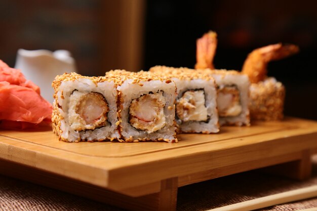 Rollo de sushi de cocina japonesa tradicional con arroz, camarones y queso crema y sésamo sobre una tabla de madera