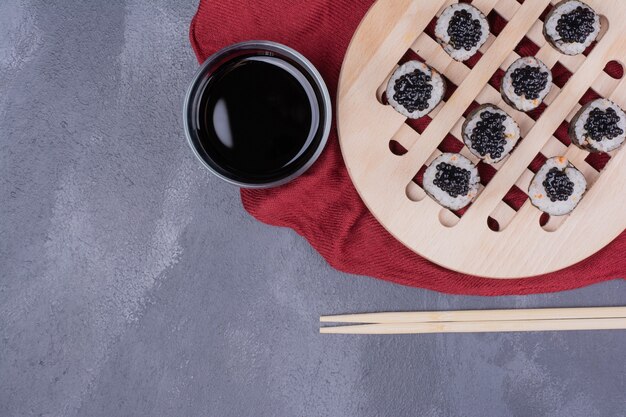 Rollo de sushi maki tradicional con palillos y salsa de soja sobre mantel rojo.