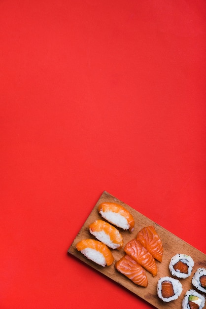 Foto gratuita rollo de sushi con salmón en la tabla de cortar contra el fondo rojo