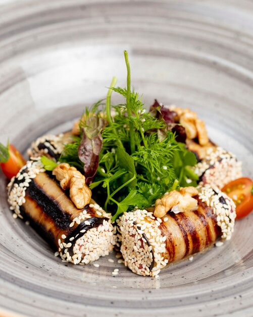 Rollos de berenjenas servidas con tomates verdes, nueces y semillas de sésamo