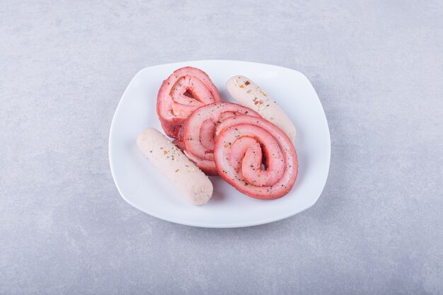 Rollos de carne ahumada y salchichas en un plato blanco.