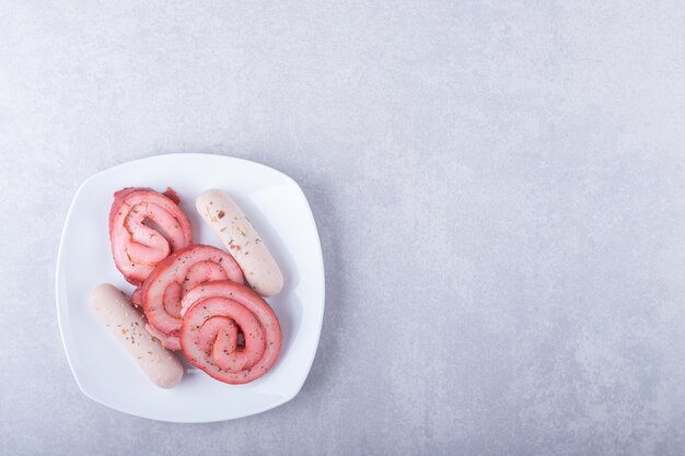 Rollos de carne ahumada y salchichas en un plato blanco.