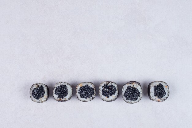 Rollos de maki decorados con caviar negro sobre fondo blanco.