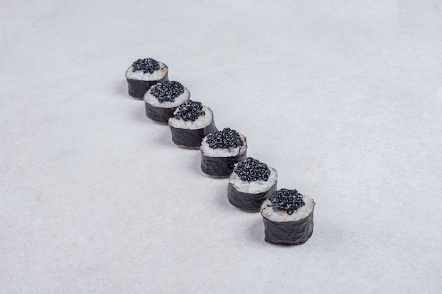 Rollos de maki decorados con caviar negro sobre fondo blanco.