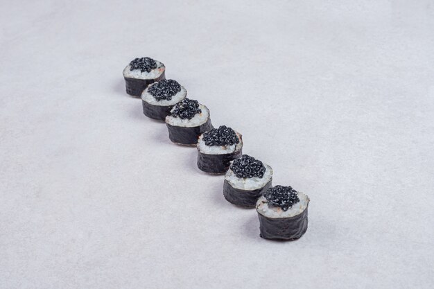 Rollos de maki decorados con caviar negro sobre fondo blanco.