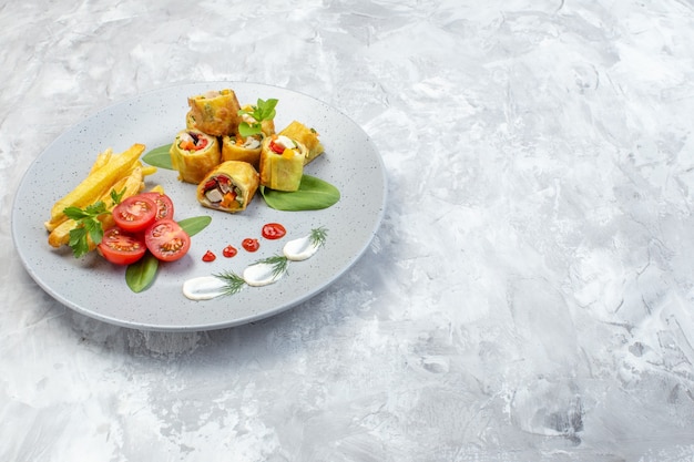 Rollos de paté de verduras de vista frontal con tomates y papas fritas dentro de la placa sobre la superficie blanca