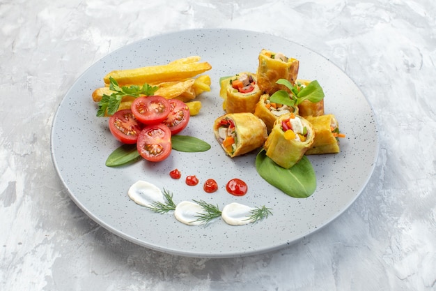 Rollos de paté de verduras de vista frontal con tomates y papas fritas dentro de la placa sobre la superficie blanca