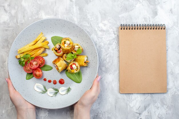 Rollos de paté de verduras de vista superior con tomates y papas fritas dentro de la placa en la superficie blanca