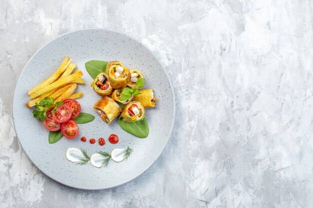 Rollos de paté de verduras de vista superior con tomates y papas fritas dentro de la placa en la superficie blanca