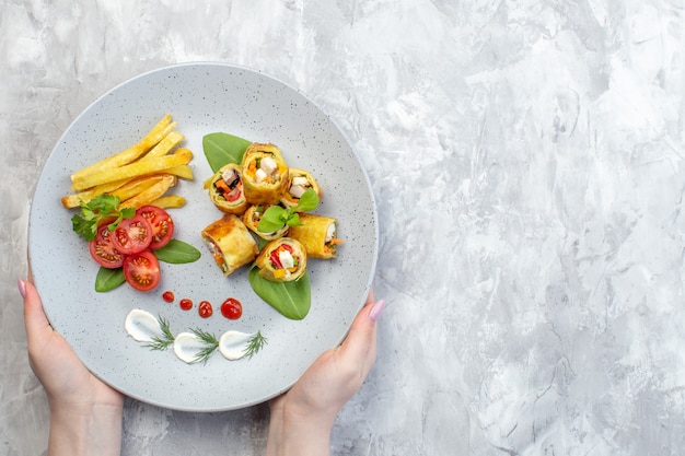 Rollos de paté de verduras de vista superior con tomates y papas fritas dentro de la placa en la superficie blanca