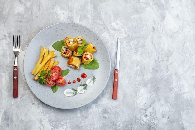 Rollos de paté de verduras de vista superior con tomates y papas fritas dentro de la placa en la superficie blanca