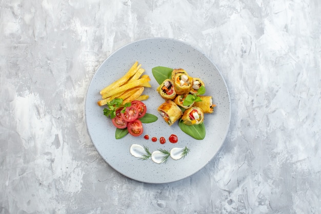 Rollos de paté de verduras de vista superior con tomates y papas fritas dentro de la placa en la superficie blanca