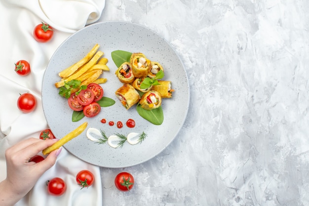 Rollos de paté de verduras de vista superior con tomates y papas fritas dentro de la placa en la superficie blanca