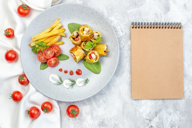 Rollos de paté de verduras de vista superior con tomates y papas fritas dentro de la placa en la superficie blanca
