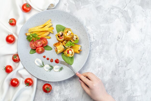 Rollos de paté de verduras de vista superior con tomates y papas fritas dentro de la placa en la superficie blanca