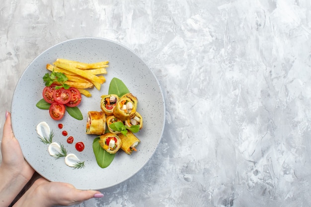 Rollos de paté de verduras de vista superior con tomates y papas fritas dentro de la placa en la superficie blanca