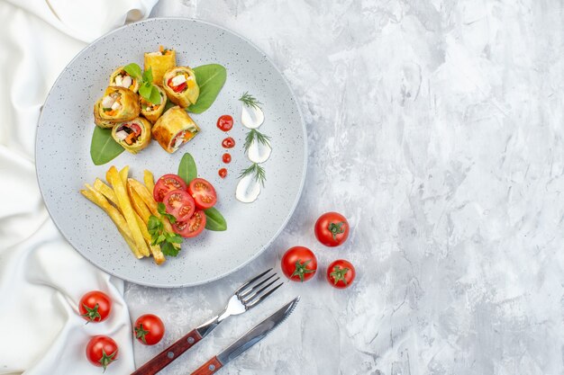 Rollos de paté de verduras de vista superior con tomates y papas fritas dentro de la placa en la superficie blanca