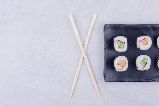 Rollos de sake maki con salmón y aguacate en una fuente de cerámica negra.