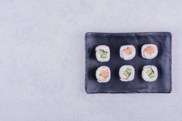 Rollos de sake maki con salmón y aguacate en fuente de cerámica negra