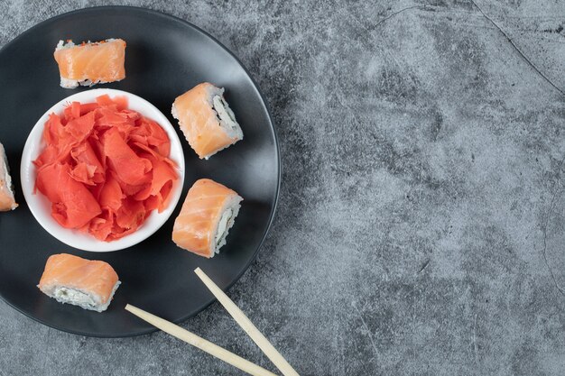 Rollos de salmón en bandeja negra con jengibre rojo marinado.