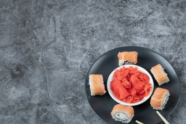 Rollos de salmón en plato negro con jengibre rojo marinado.