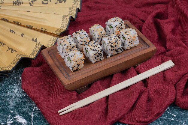 Rollos de sushi de Alaska servidos en bandeja de madera con palillos y abanico japonés.
