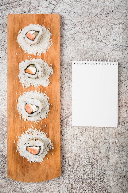 Rollos de sushi en la bandeja de madera con la libreta espiral en blanco en fondo rústico