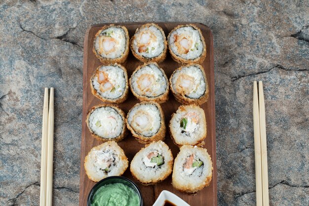 Rollos de sushi caliente frito con queso crema, wasabi y salsa de soja sobre una tabla de madera.