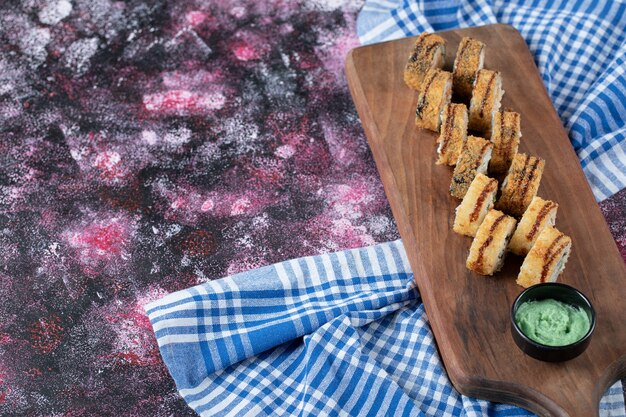 Rollos de sushi caliente frito sobre una tabla de madera con salsa de wasabi.