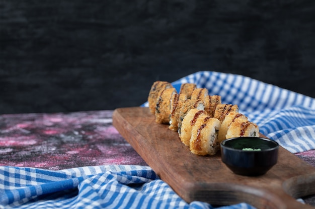 Rollos de sushi caliente frito sobre una tabla de madera con salsa de wasabi.