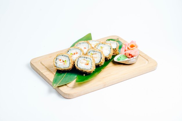 Rollos de sushi calientes con tempura y aguacate servidos en hojas sobre tabla de madera