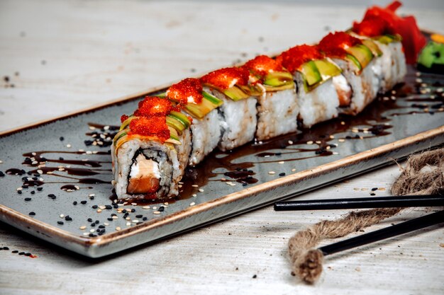 rollos de sushi cubiertos con aguacate, crema y tobiko rojo y salsa de soja