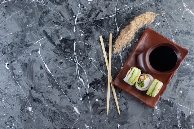 Rollos de sushi de dragón verde colocados en un plato marrón con salsa de soja.