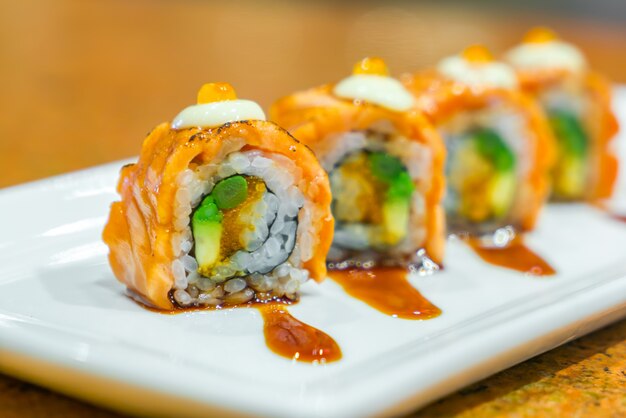 Rollos de sushi japonés con salmón fresco crudo en un plato blanco.