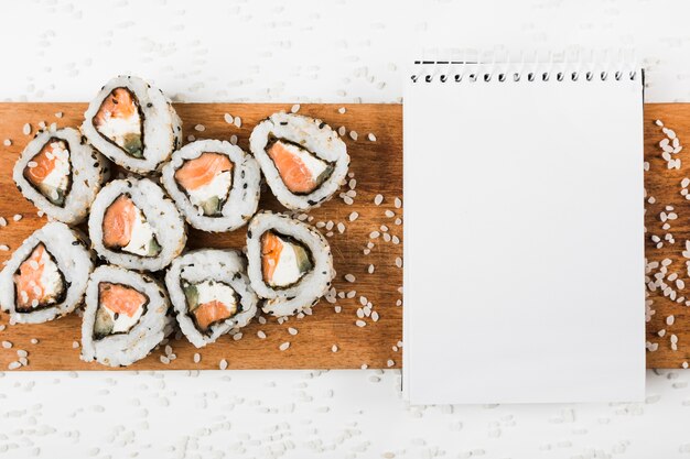 Rollos de sushi y libreta espiral en bandeja de madera con salpicaduras de arroz crudo