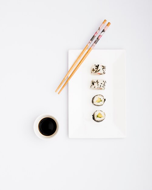 Rollos de sushi listos para comer en un plato blanco con palillos y salsa de soja aislados sobre fondo blanco