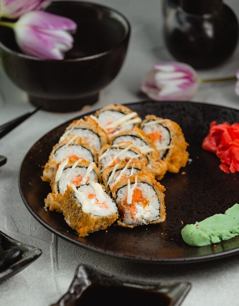 Rollos de sushi en placa blac con tulipanes alrededor.