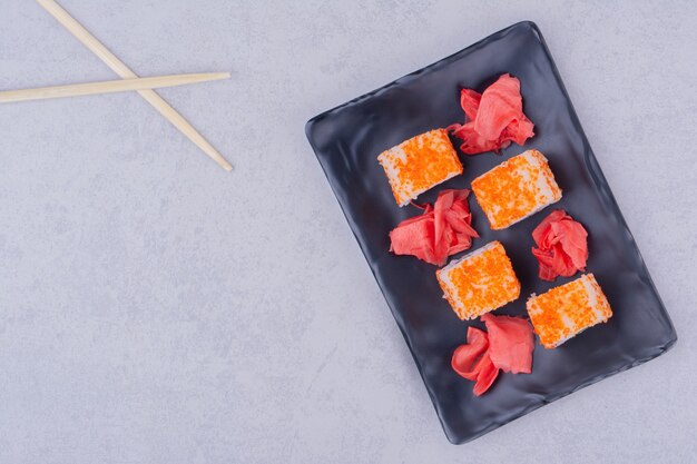 Rollos de sushi con salmón en un plato de cerámica negra.