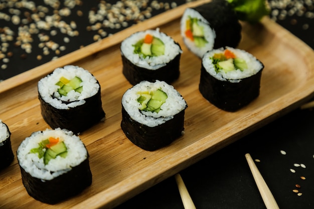 Rollos de sushi servido en plato de madera con ingredientes clásicos vista cercana