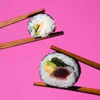 Foto gratuita rollos de sushi sujeto por palillos sobre un fondo rosa