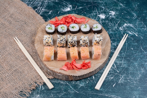Rollos de sushi surtidos servidos en bandeja de madera con jengibre encurtido y palillos.