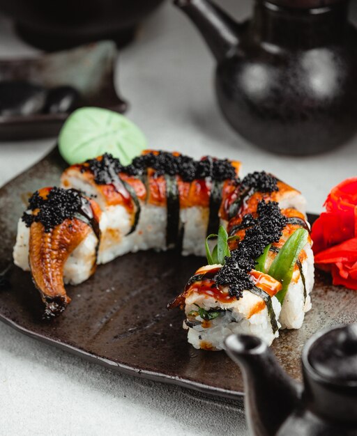 Rollos de sushi unagi con caviar negro sobre placa negra.