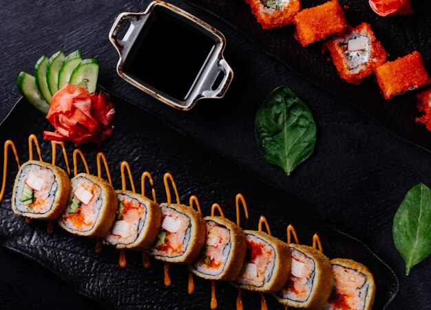 Rollos de sushi variedades en plato negro con salsa de soja.