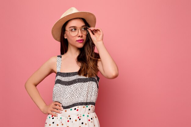 Romántica hermosa joven vestida con sombrero de verano y vestido brillante, con gafas posando