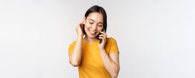 Romántica y linda chica asiática responde llamadas telefónicas hablando por móvil sonriendo coqueta de pie gritando