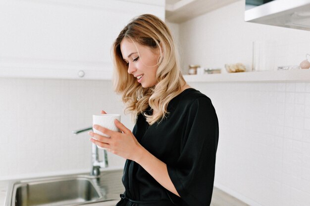 Romántica mujer europea con hermoso peinado sentada en la mesa de la cocina