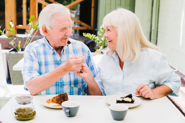 Romántica pareja de ancianos sentados en la cafetería en la terraza y disfrutar de pasteles