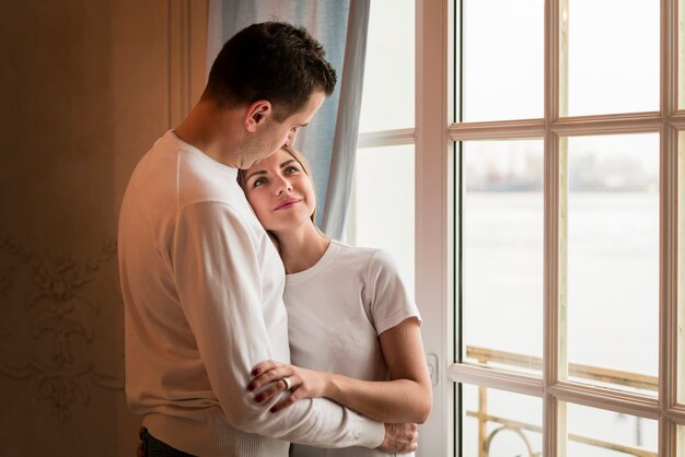 Romántica pareja feliz abrazada junto a la ventana